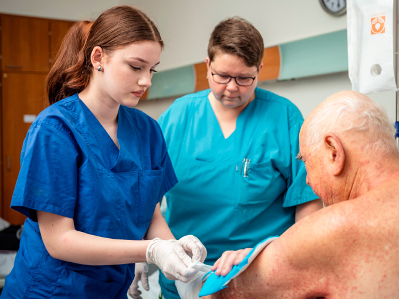 Schülerpraktikantin hilft Schwester beim eincremen eines Patienten