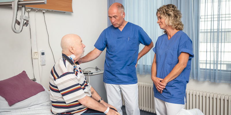 Chefarzt mit Schwester reden mit Patient am Bett