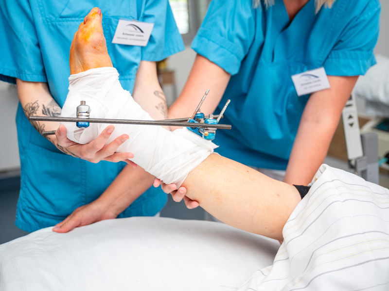 Schwestern halten den operierten Fuß eines Patienten hoch