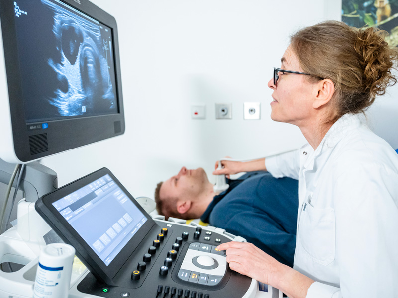 Ärztin führt Sonografie der Schilddrüse bei einem Patienten durch